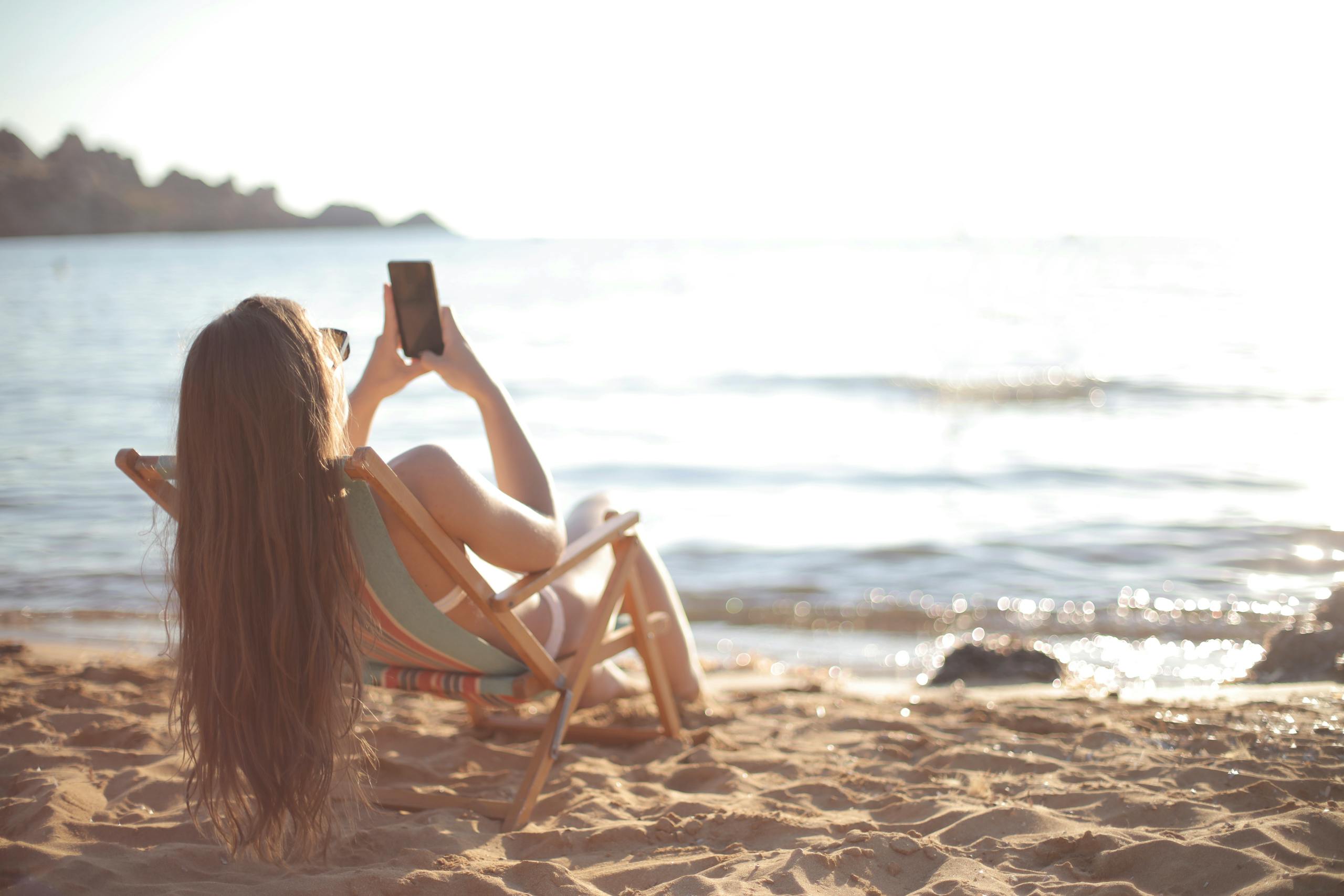 Woman in bikini relaxes on a beach chair by the ocean, capturing summer memories.