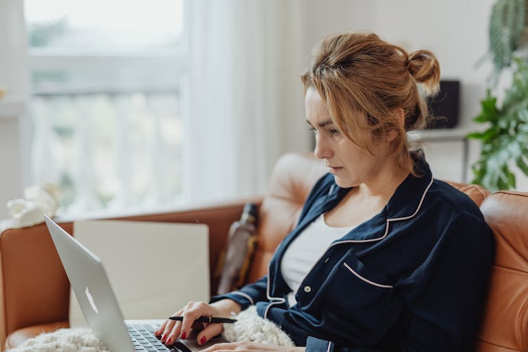 Woman in pajamas working on a laptop from a cozy home environment, focused on her task.
