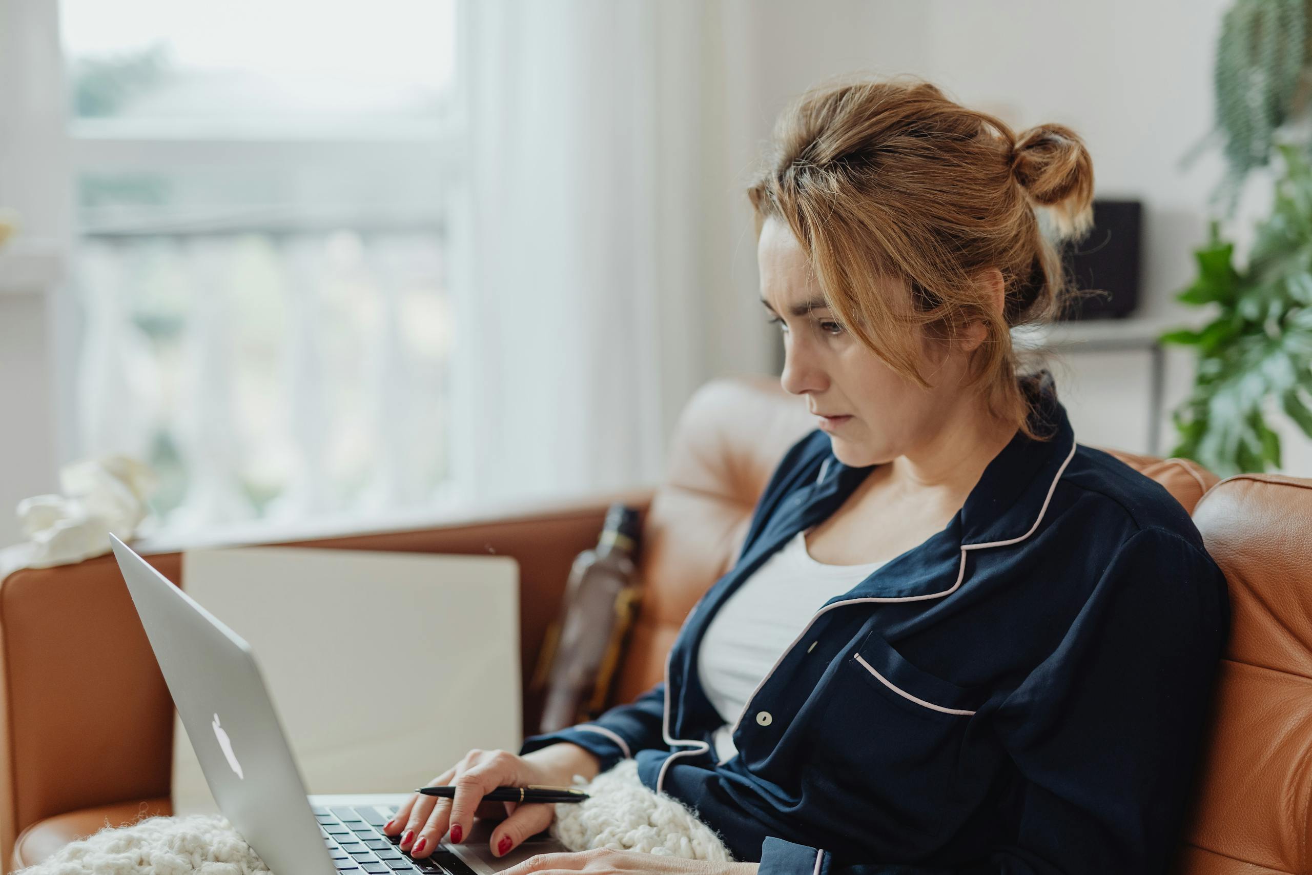 Woman in pajamas working on a laptop from a cozy home environment, focused on her task.