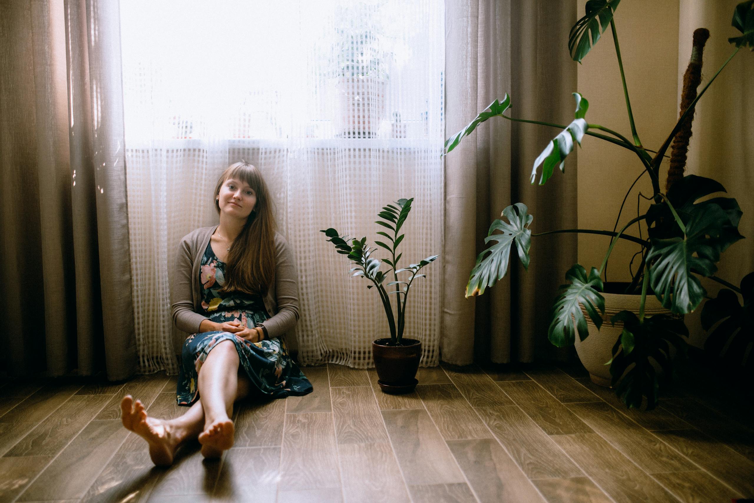 Woman sitting by a window with plants, exuding calmness and serenity indoors.