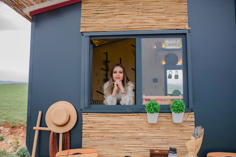 Woman smiling through a window of a modern, rustic cabin with decor.