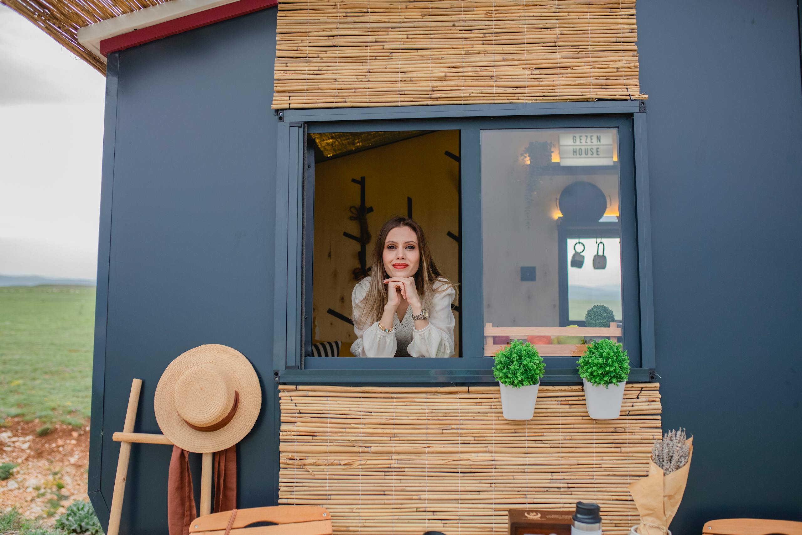 Woman smiling through a window of a modern, rustic cabin with decor.