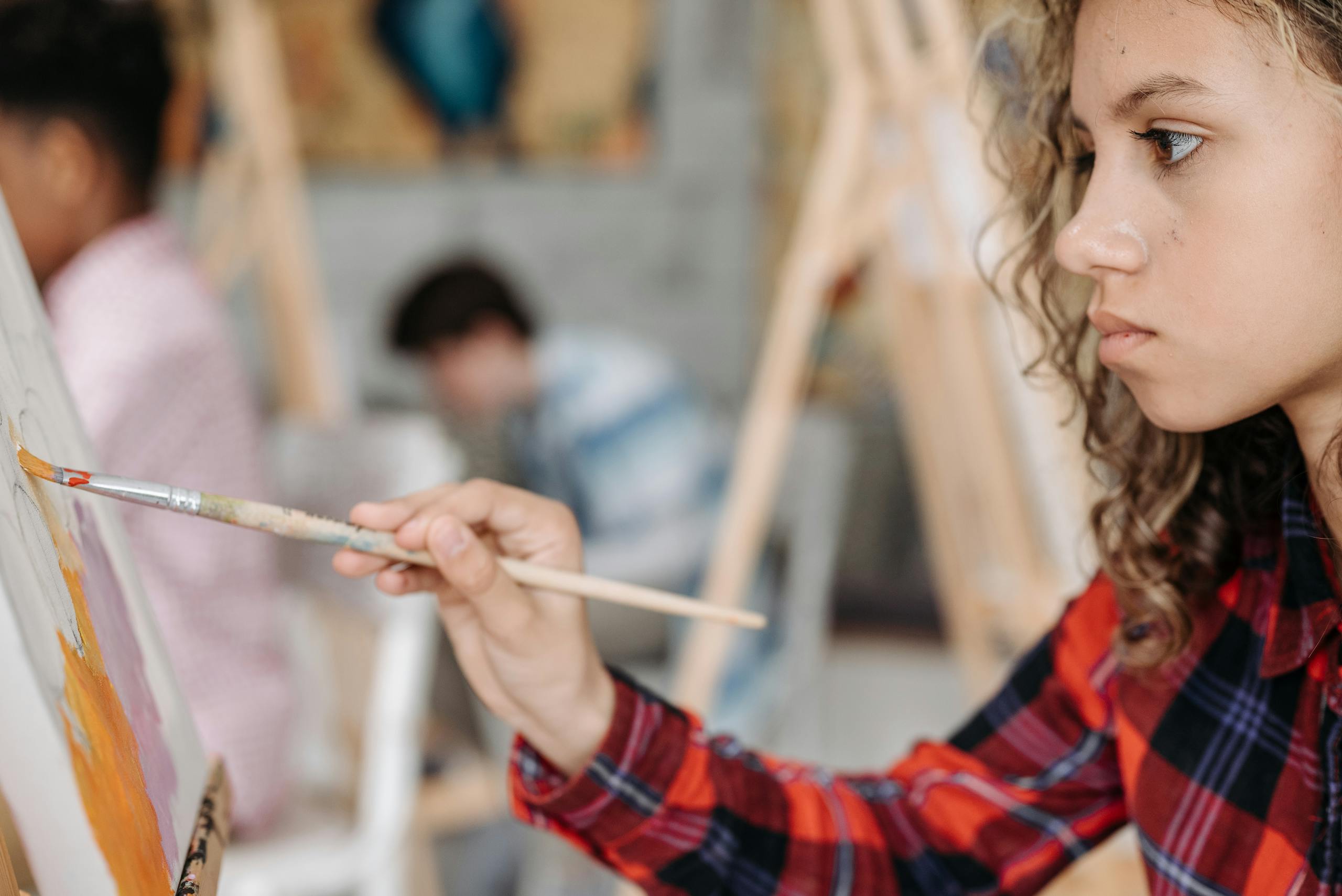 Young girl deeply focused on painting at an art class, capturing creativity and education indoors.