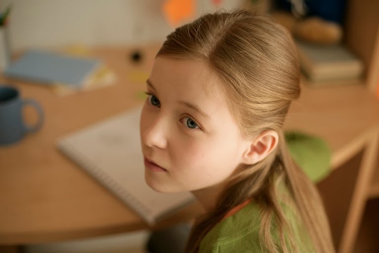 Young girl sitting at a desk in a cozy room, appearing thoughtful and pensive.