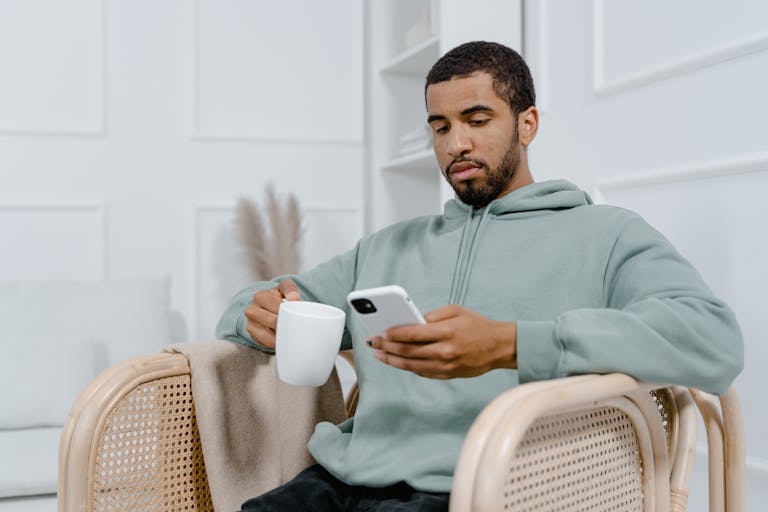 Young man in a grey hoodie sits with a coffee mug and smartphone, exuding a relaxed vibe.