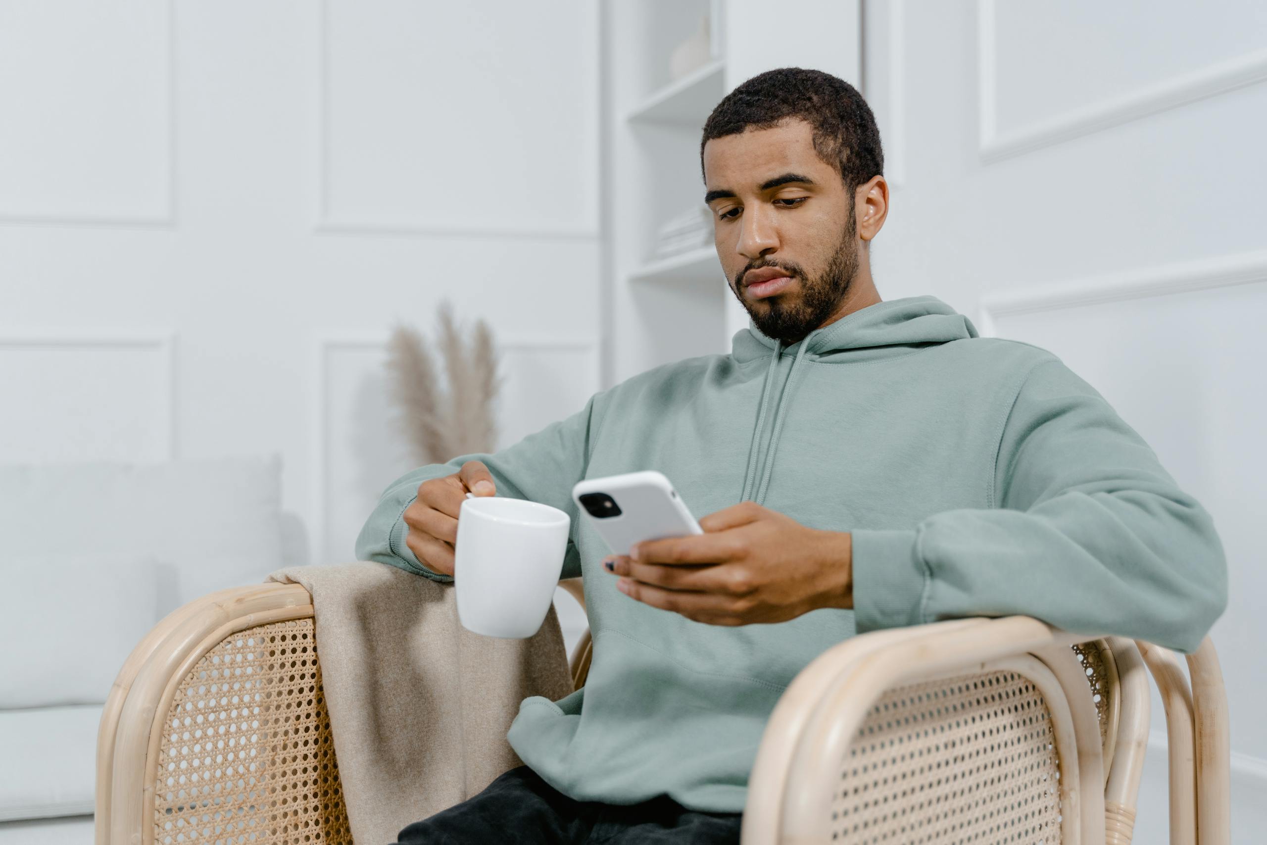 Young man in a grey hoodie sits with a coffee mug and smartphone, exuding a relaxed vibe.