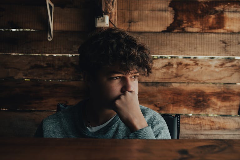 Young man sitting pensively by a wooden wall, thoughtful mood.