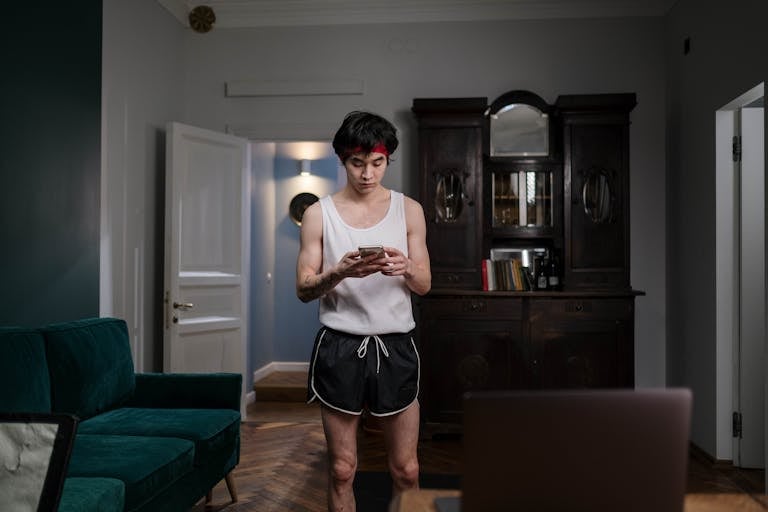 Young man standing in living room texting, dressed in sportswear.