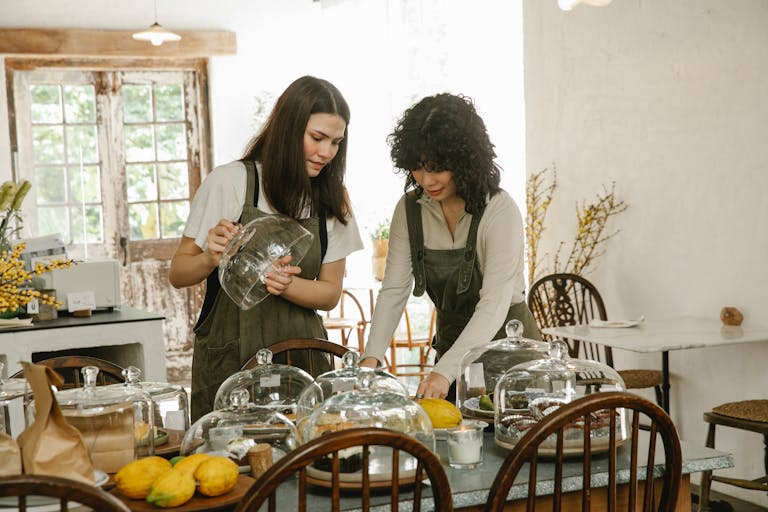 Young positive waitresses wearing aprons serving delicious fresh desserts for dinner in cafe