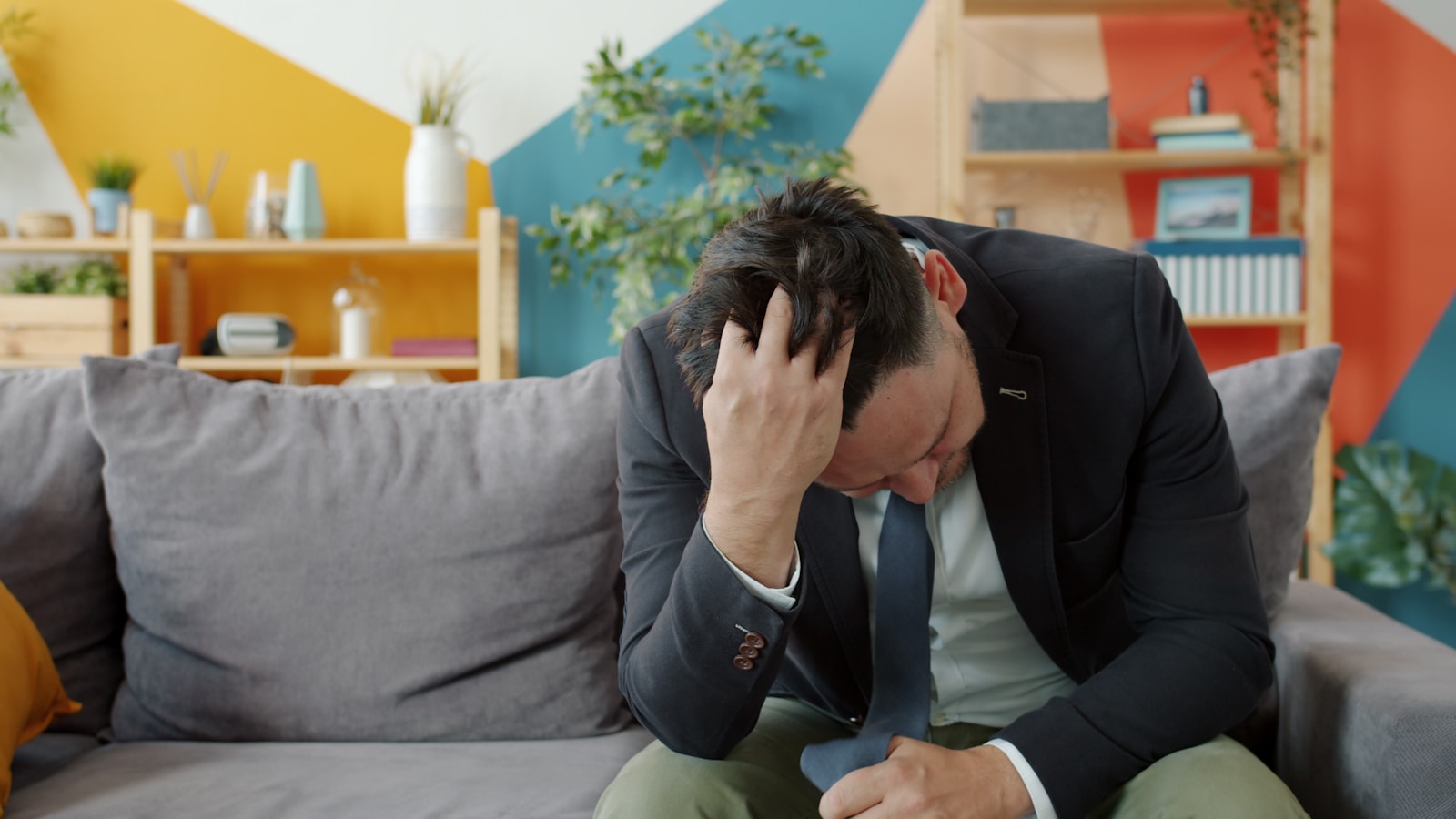 Man in suit sitting on couch with head in hands.