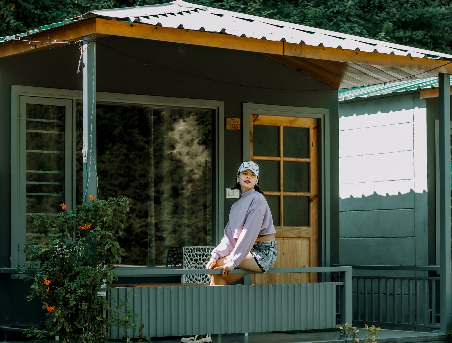 A stylish woman sitting on a porch railing, enjoying a sunny day outdoors.