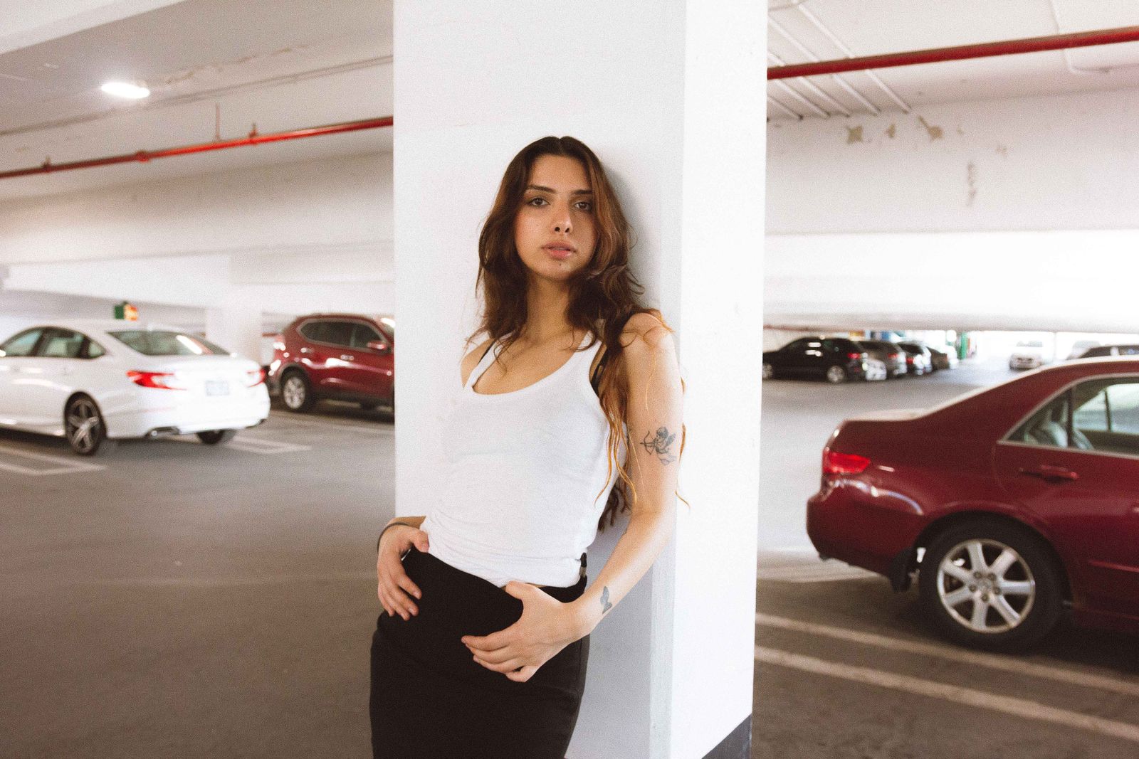 Chic woman in casual fashion posing against pillar in a parking garage. Urban style and confidence.