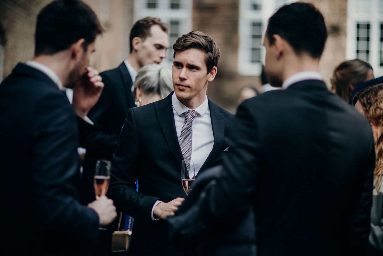 Well-dressed guests engage in conversation at an outdoor wedding reception.