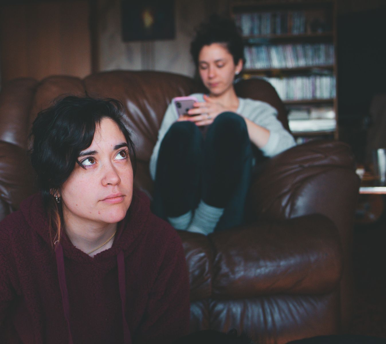 A cozy indoor scene with two women, one using a phone and the other gazing thoughtfully.