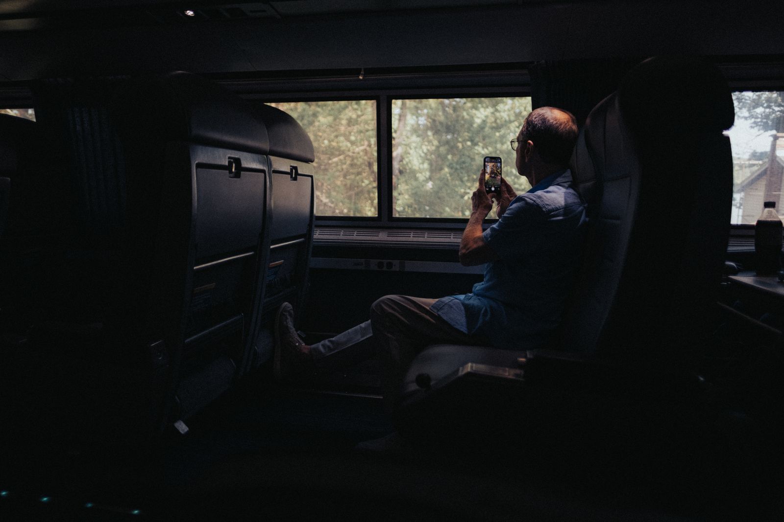 Senior man captures scenic views from a train window using a smartphone.