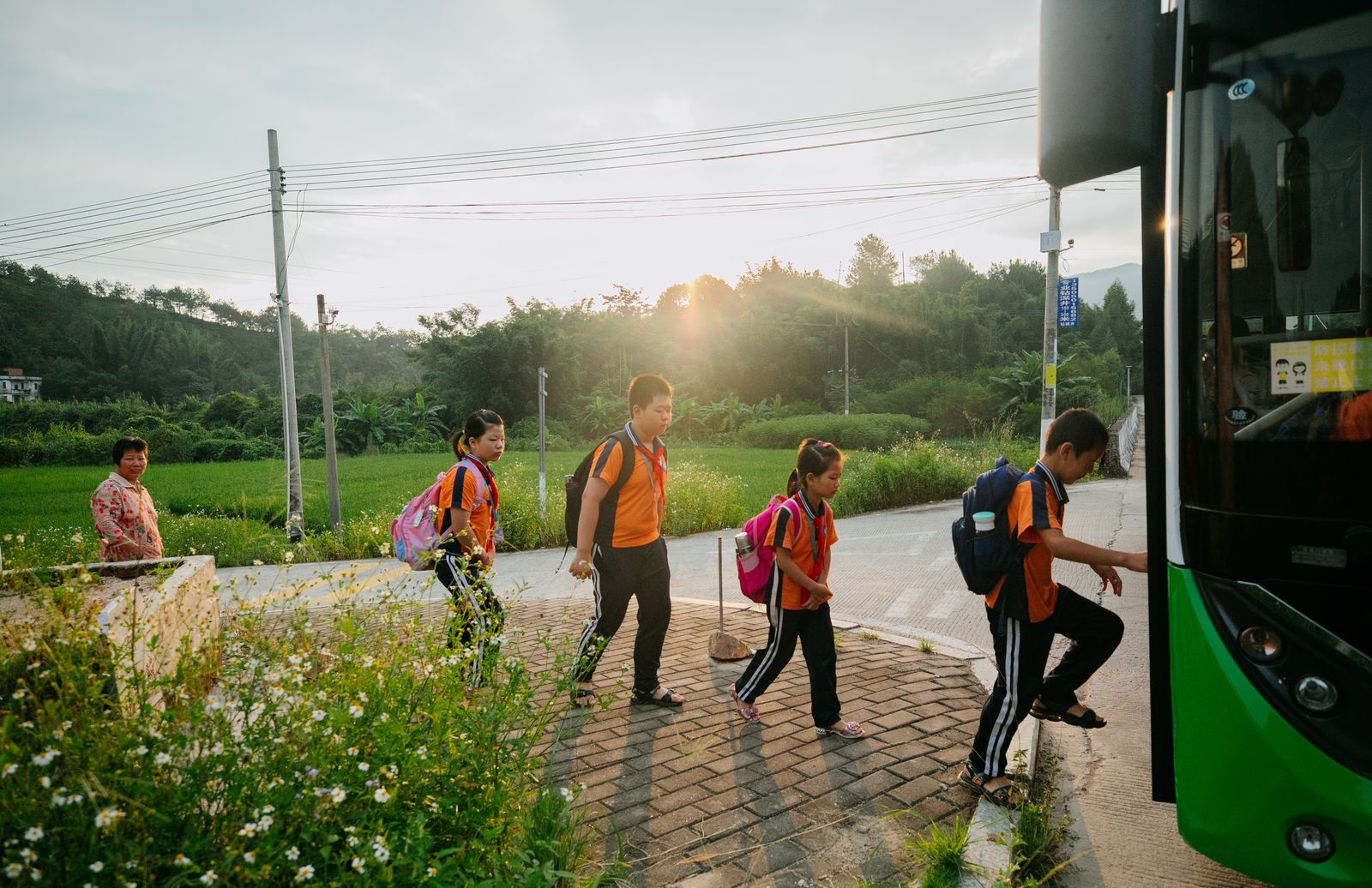 Group of Asian students in uniforms boarding a school bus at sunrise, showcasing a typical morning.