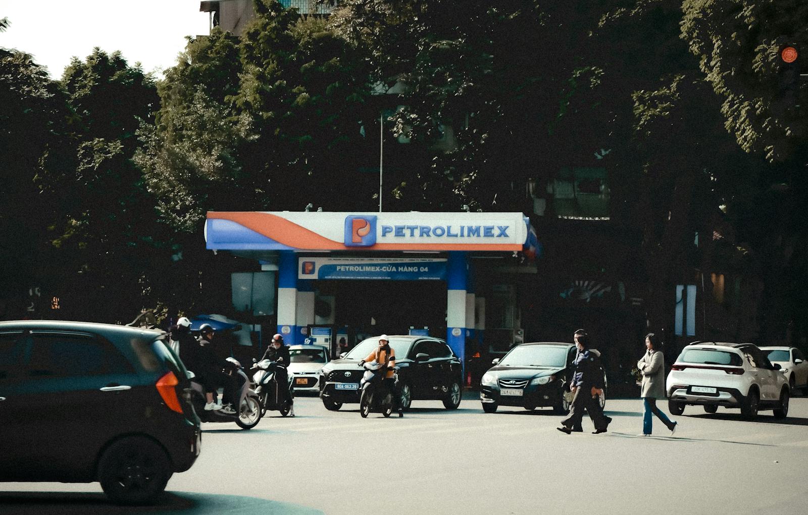 Busy street scene with vehicles and pedestrians at a Petrolimex gas station under daylight.