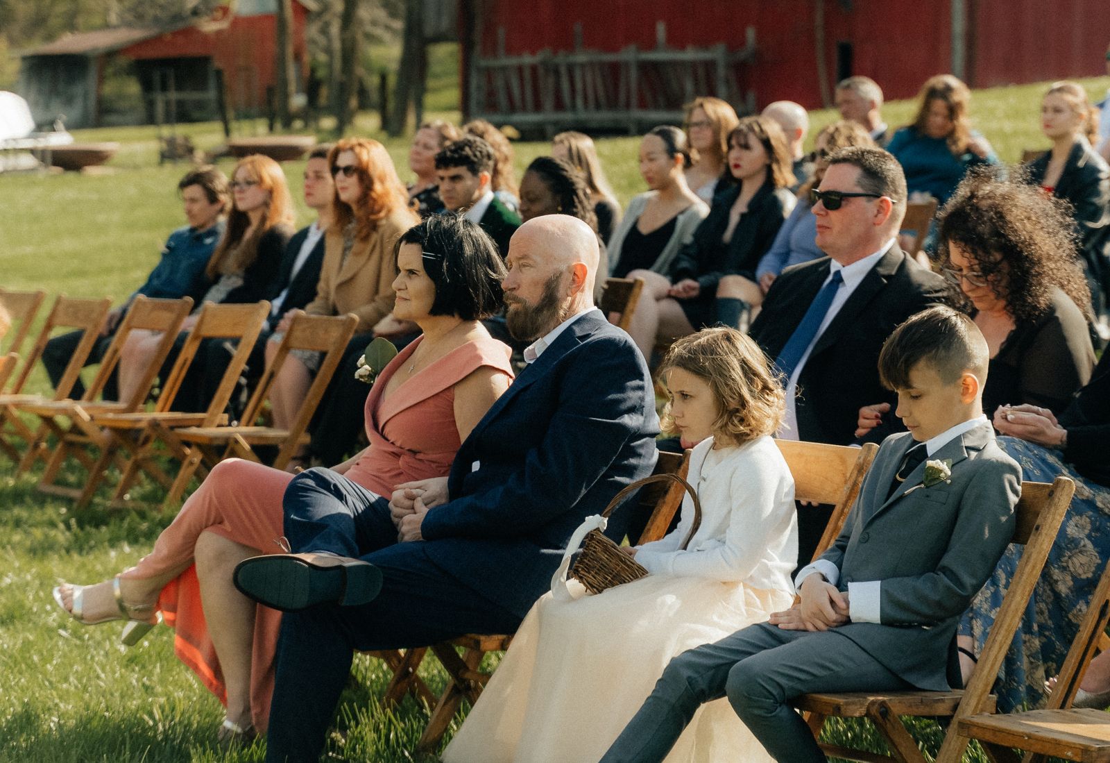 Guests seated on wooden chairs at a sunny outdoor wedding ceremony in Indianapolis.