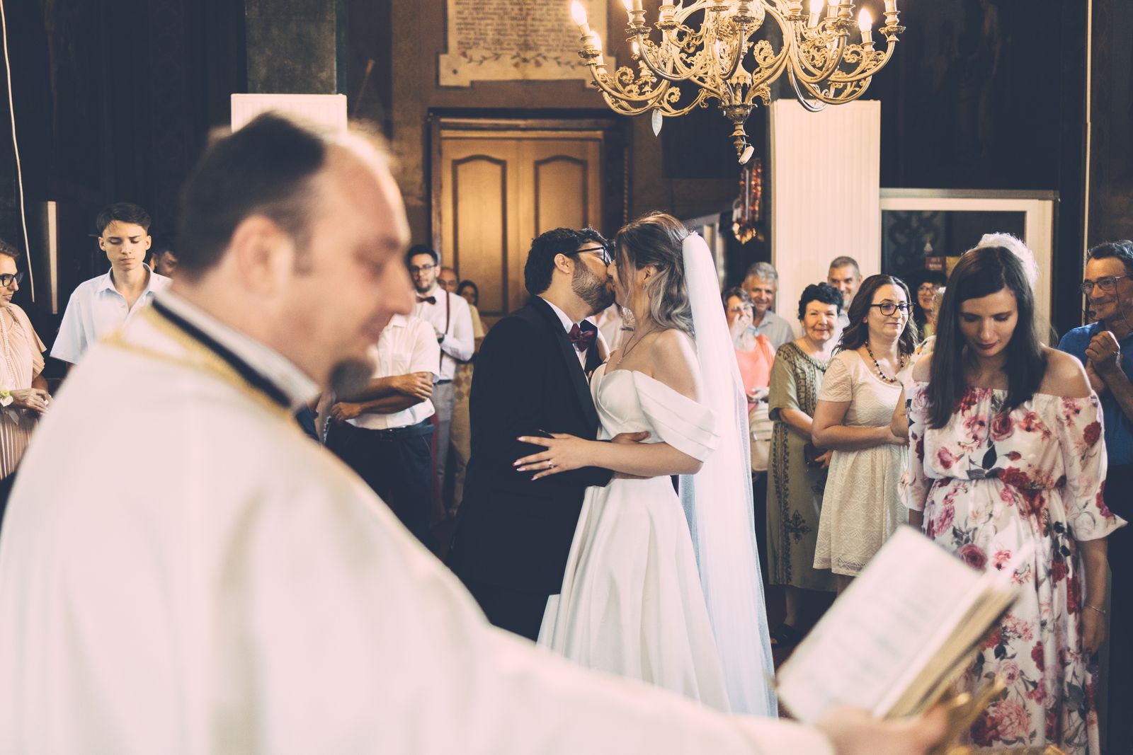 Bride and groom share a kiss during wedding ceremony in an elegant church setting as guests watch with joy.