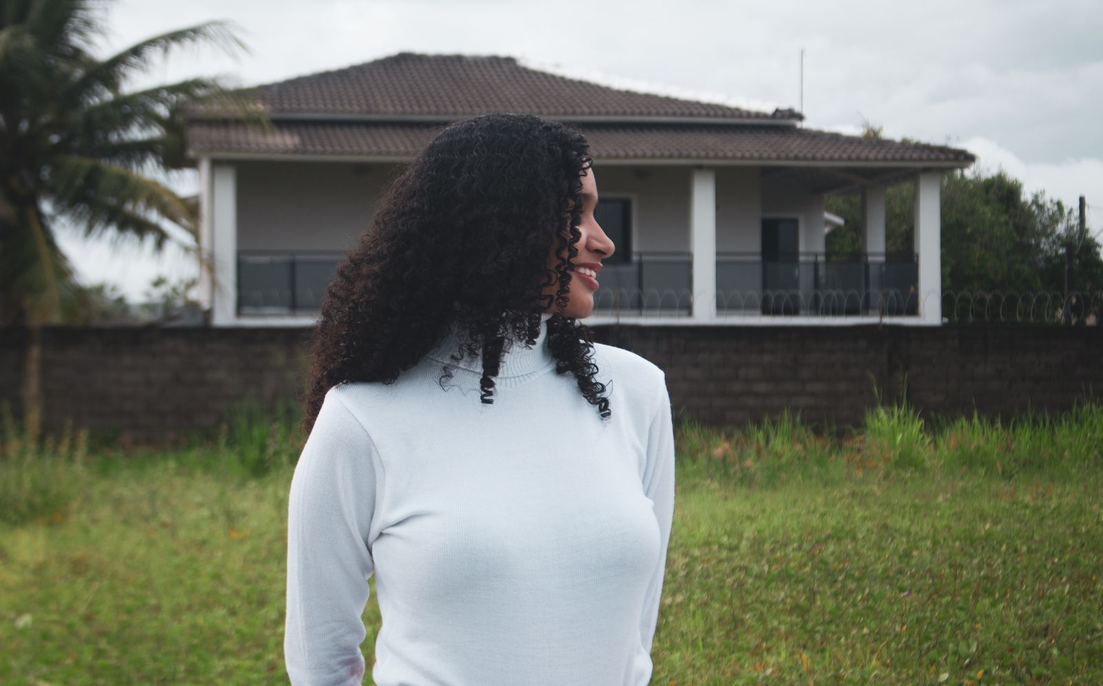 A woman smiles while standing outdoors in front of a modern house.