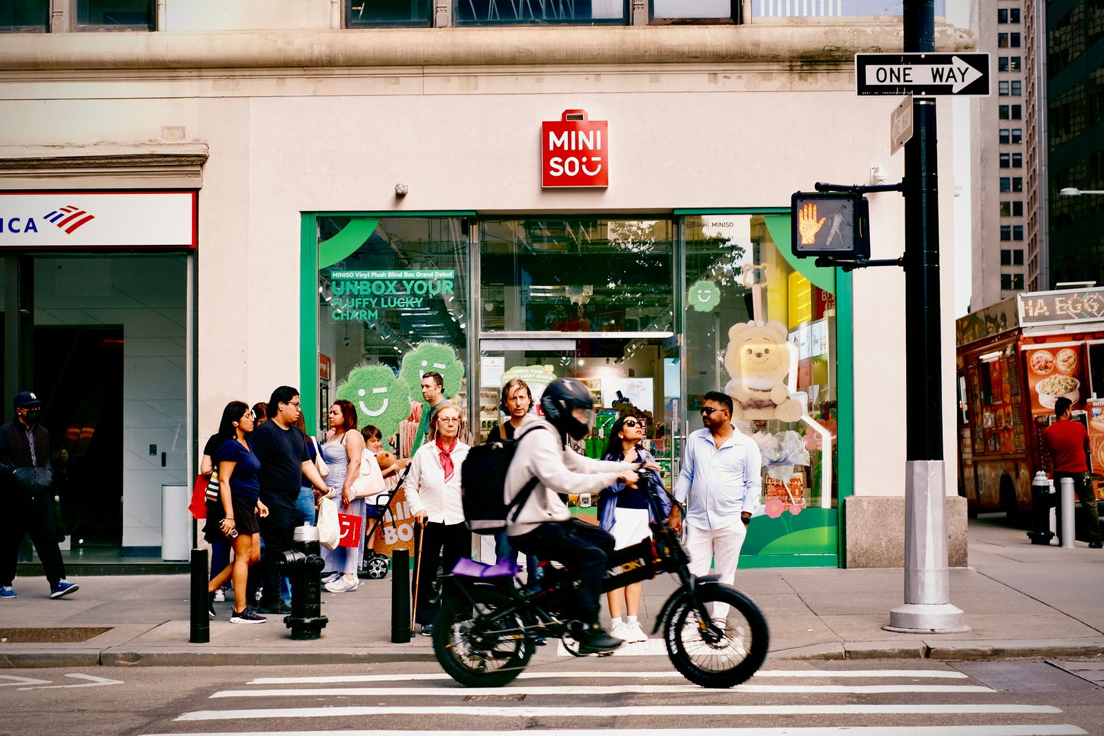 Dynamic street view in New York City with people and a cyclist outside Miniso store.