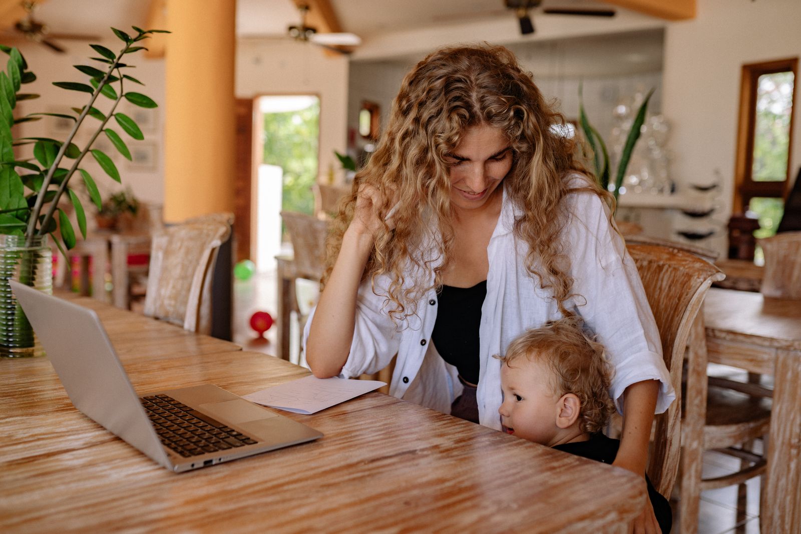 A mother and her toddler enjoy a moment together at home, with a laptop on the table.