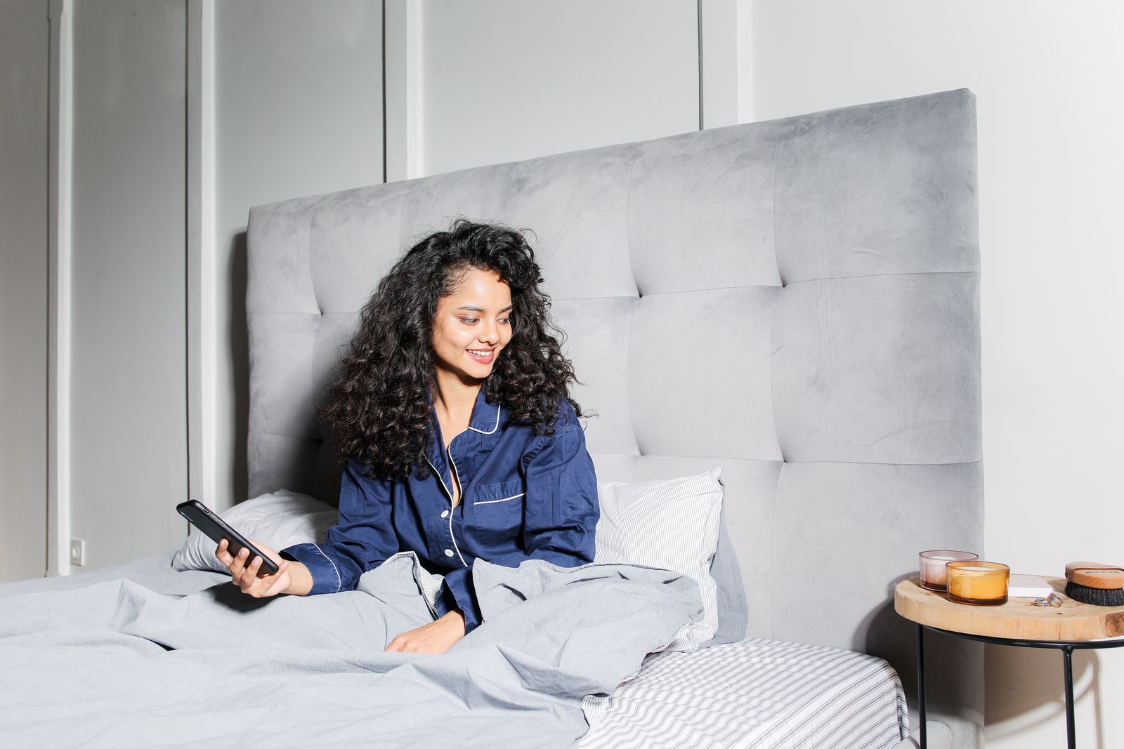 Woman in pajamas relaxing in bed with a smartphone, enjoying a cozy morning at home.