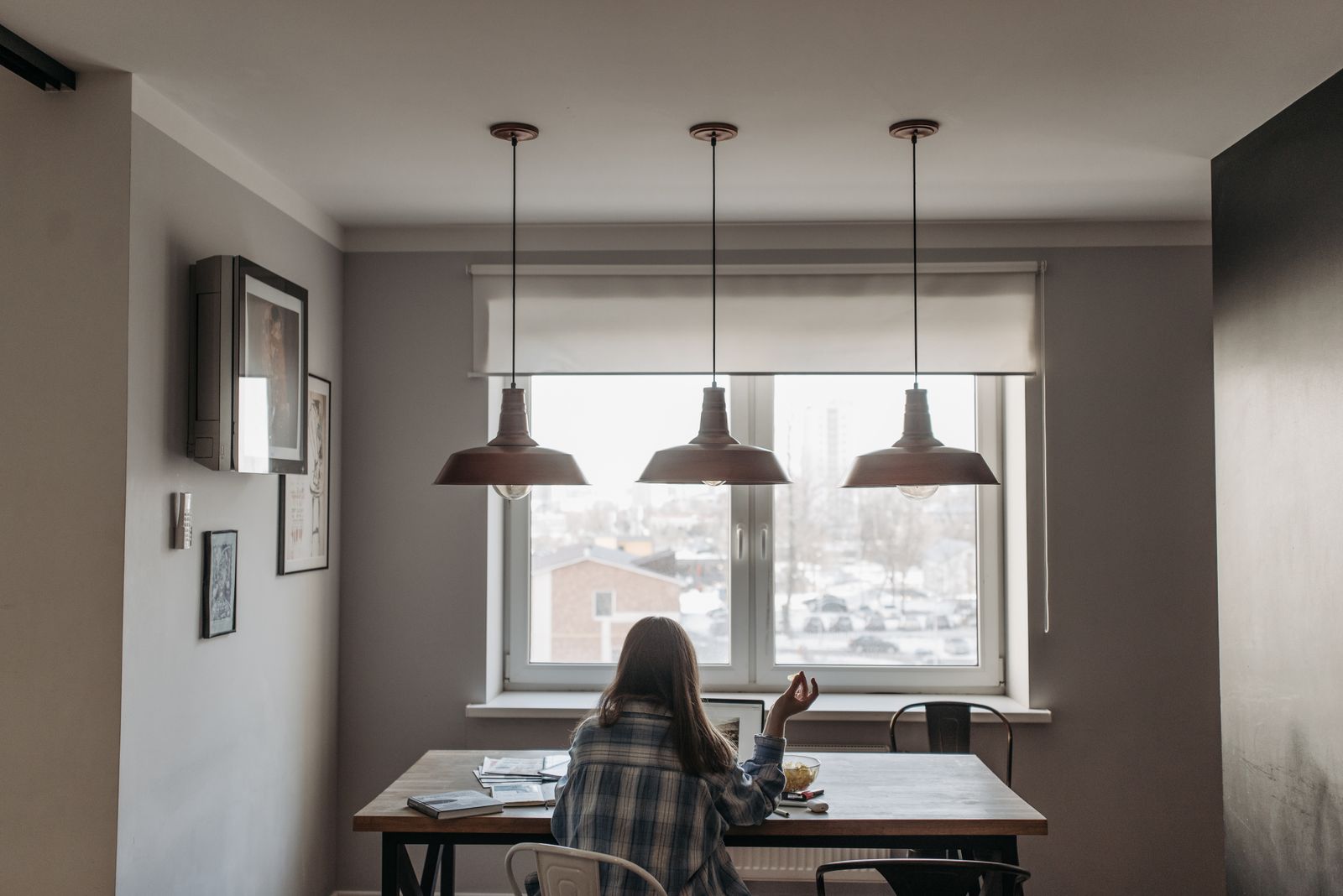 Person working from home in a modern dining room setup with laptop and snacks on the table.