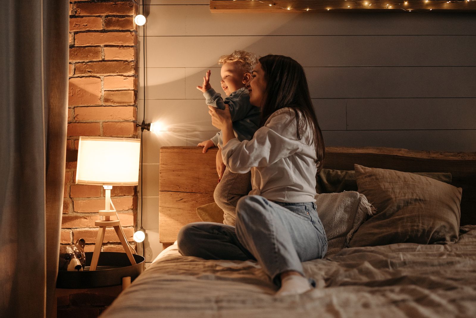 A mother lovingly plays with her child in a warmly lit bedroom, creating a cozy atmosphere.