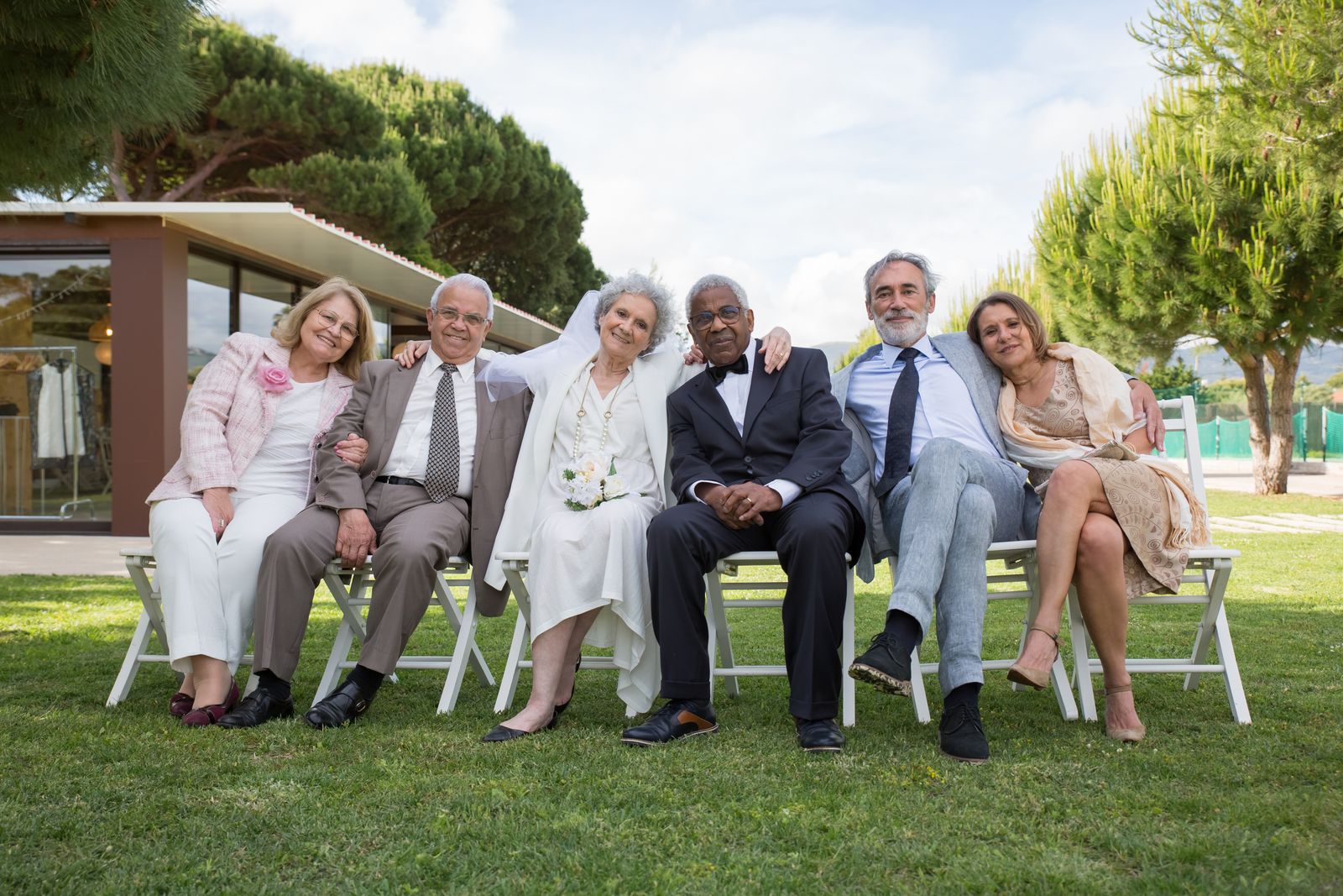 A joyful outdoor wedding celebration featuring senior couples sitting on chairs, embracing and smiling.