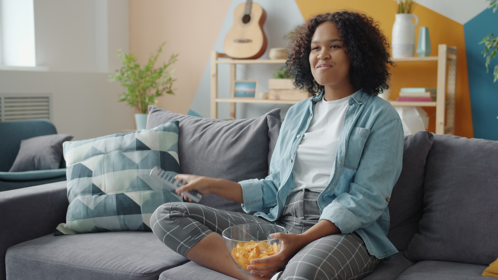 Young woman watching TV and eating snacks on couch.