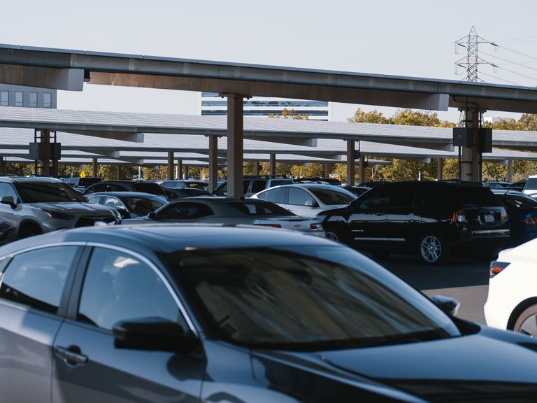 A busy outdoor parking lot filled with various parked cars under solar panel structures.