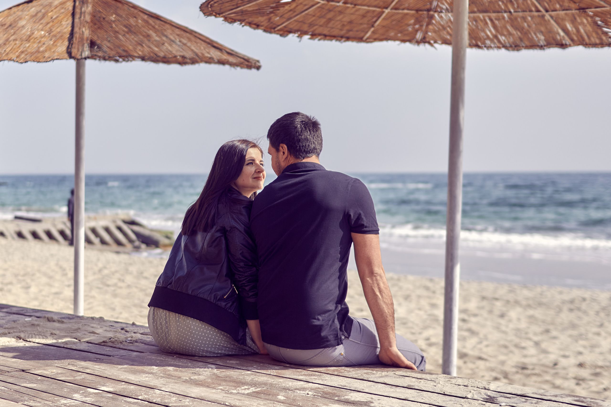 A couple enjoying a romantic moment on the sandy beach of Odessa under the shade of straw umbrellas.