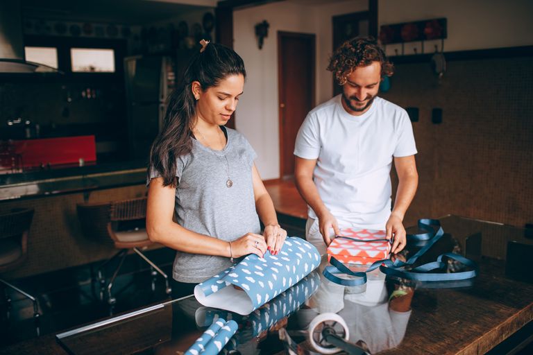 A couple joyfully wrapping presents on a table in a warm and cozy home environment.