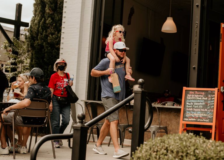 A father carrying his daughter on shoulders outside a cafe, enjoying a sunny day.