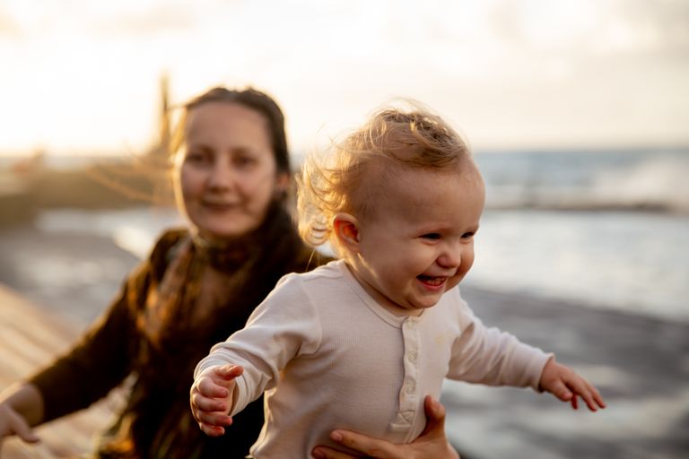 A happy mother and baby enjoying a sunny day by the sea, capturing their bond.