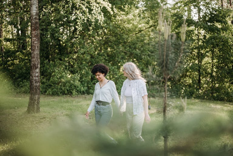 A joyful couple holding hands while walking outdoors, embraced by lush greenery.