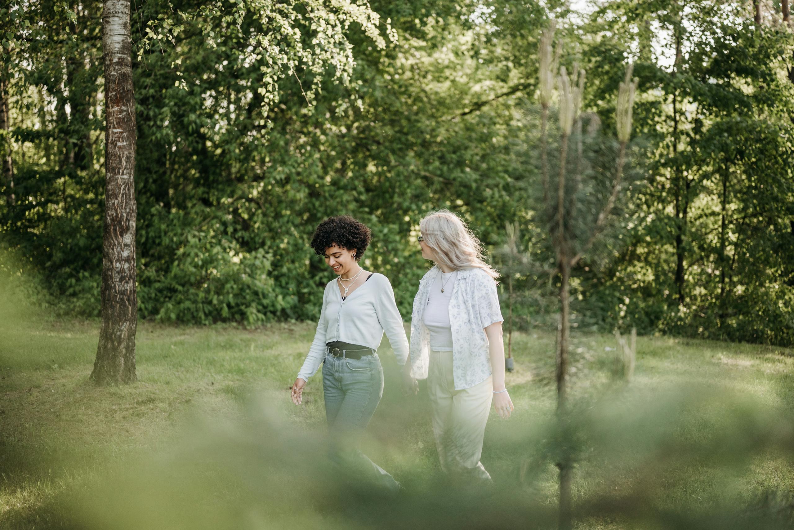 A joyful couple holding hands while walking outdoors, embraced by lush greenery.