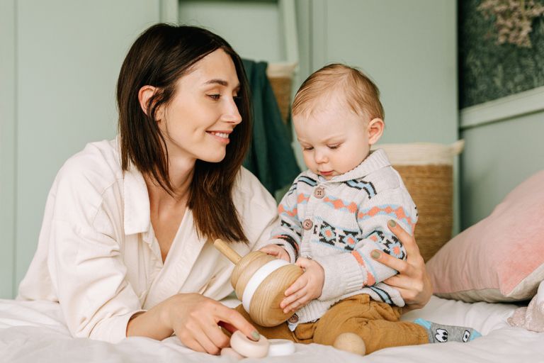 A loving mother and toddler share a playful moment indoors, focusing on a wooden toy.