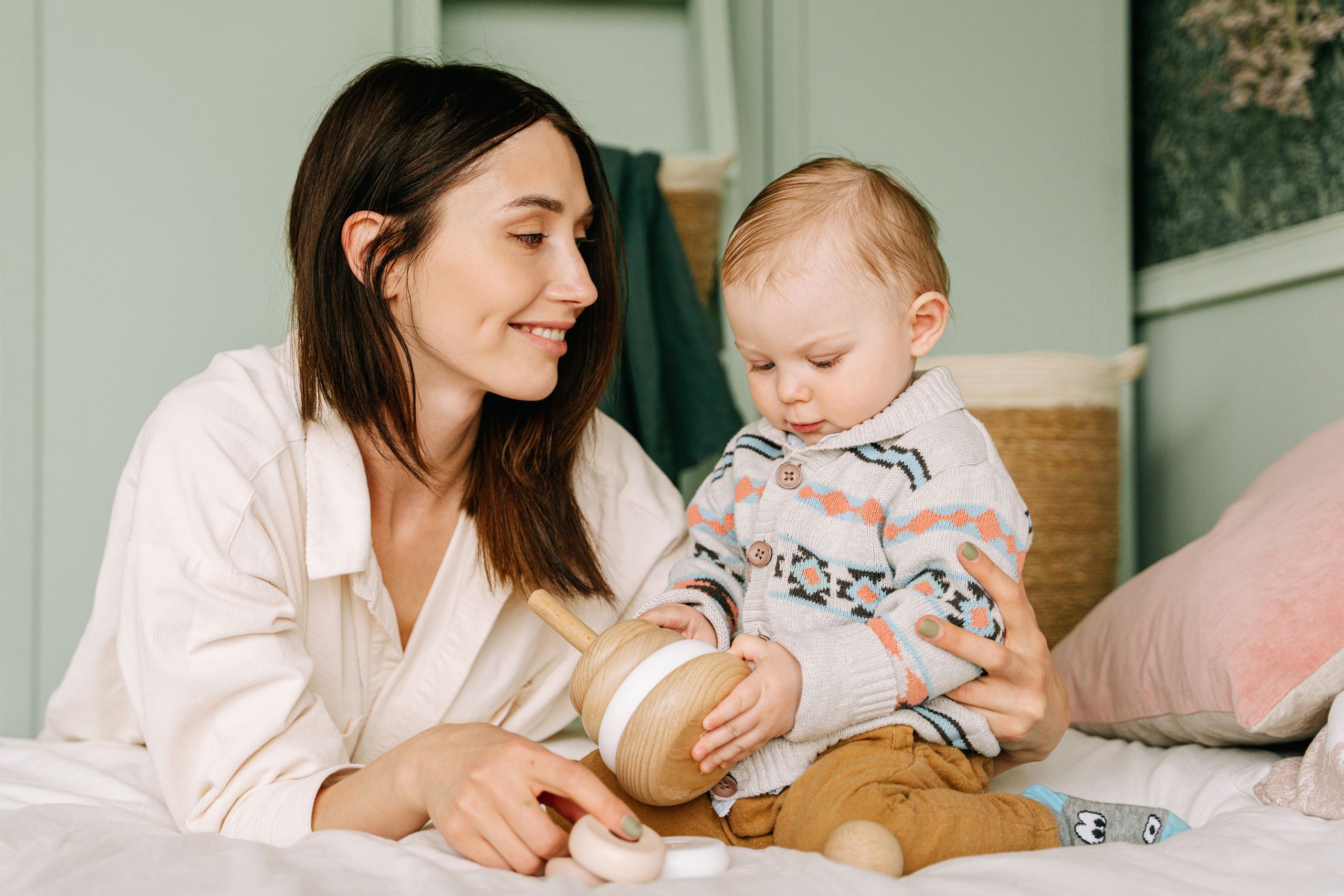 A loving mother and toddler share a playful moment indoors, focusing on a wooden toy.