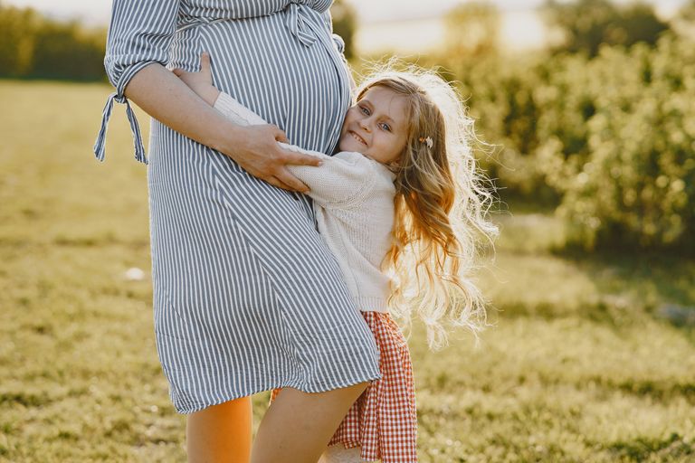 A pregnant mother enjoying a tender moment with her daughter in a sunny outdoor setting.