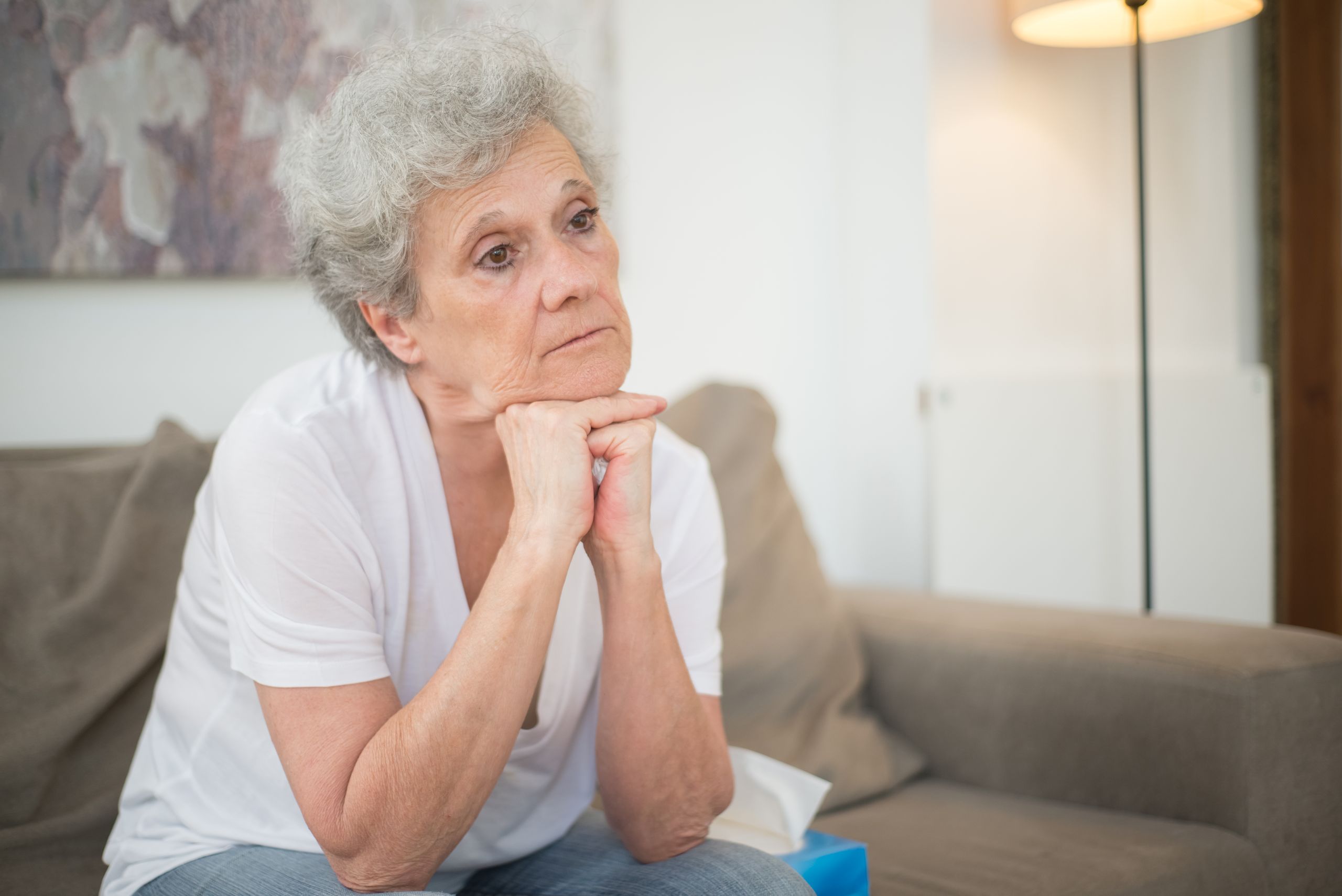 A thoughtful senior woman with gray hair sitting indoors, reflecting.