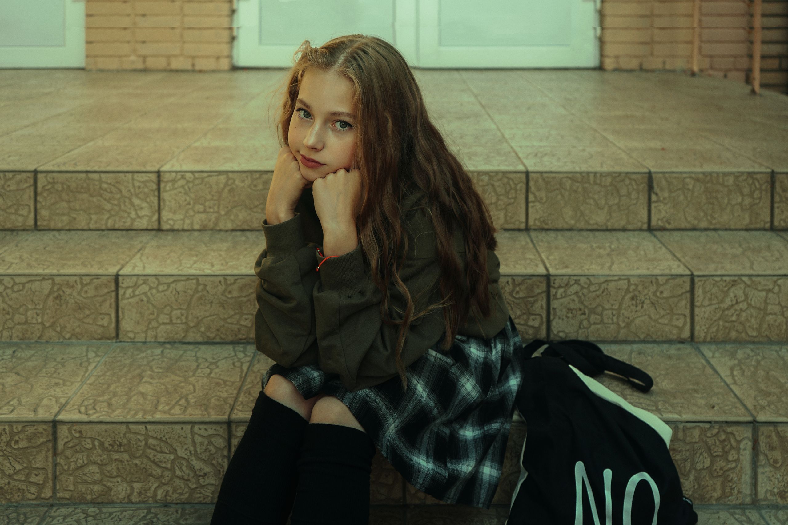 A thoughtful teenage girl sits on stairs, resting her chin on her hands.