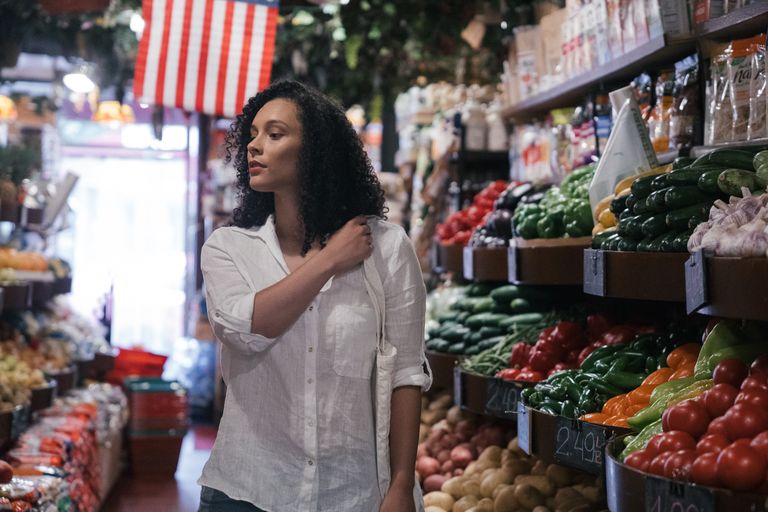A woman exploring colorful fresh produce in a bustling grocery store aisle.