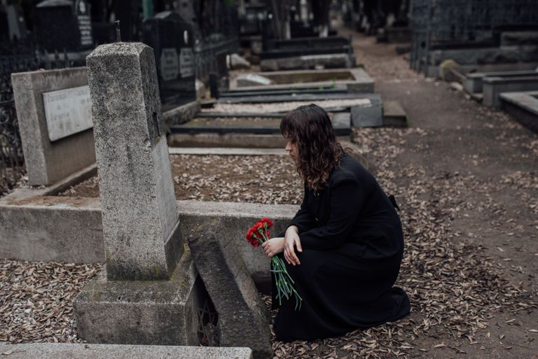 A woman in mourning holds red flowers in a quiet cemetery.