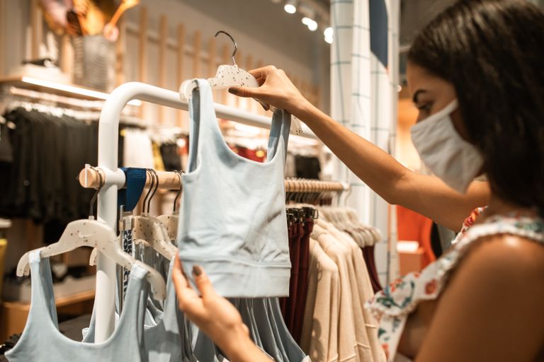 A woman wearing a face mask browses sports bras in an apparel store, embracing the new normal.
