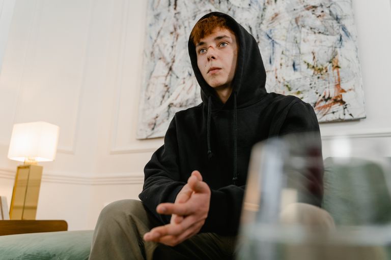 A young man wearing a hoodie sits pensively in a therapy setting, focusing on mental health.
