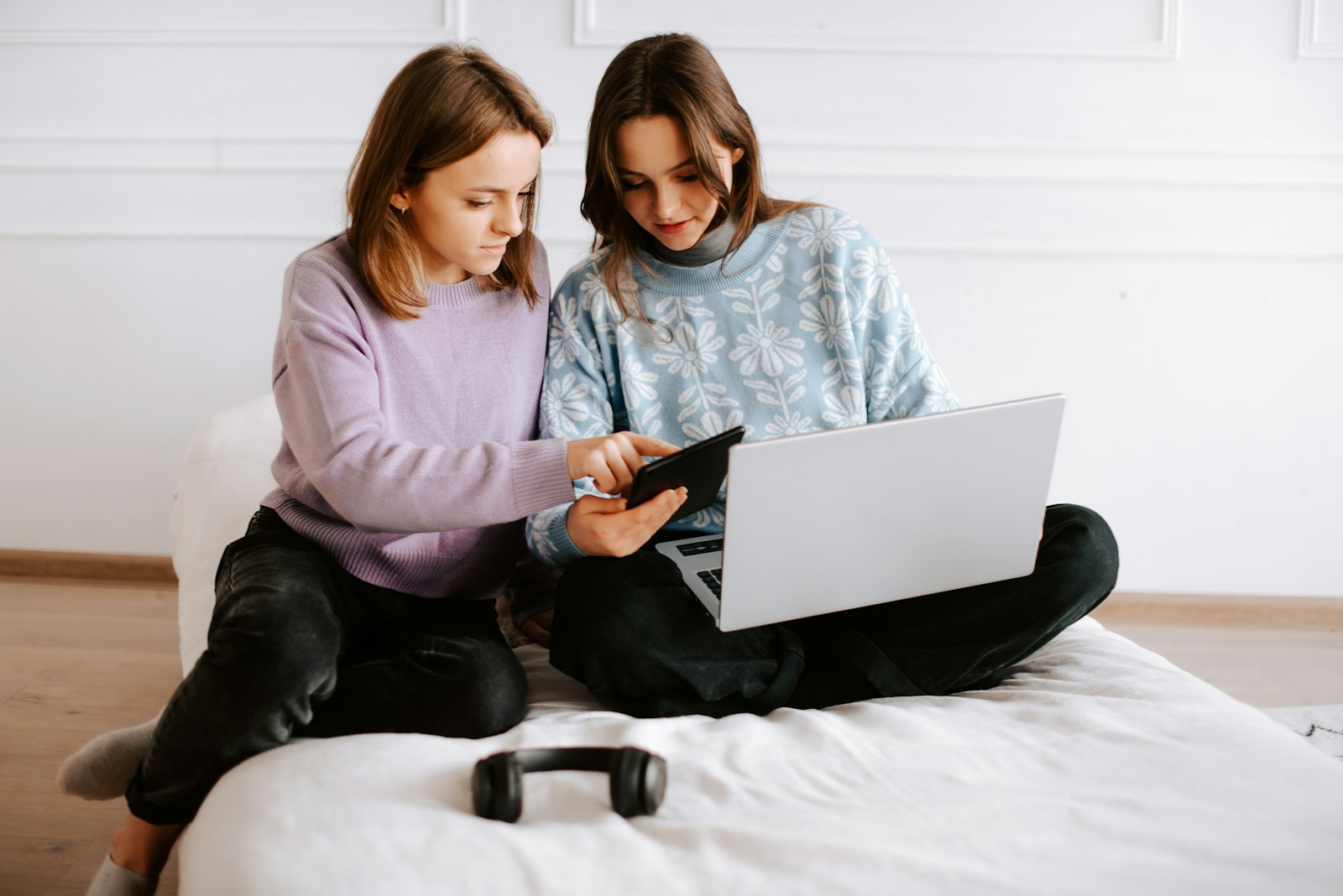 two girls sitting on a bed looking at a laptop