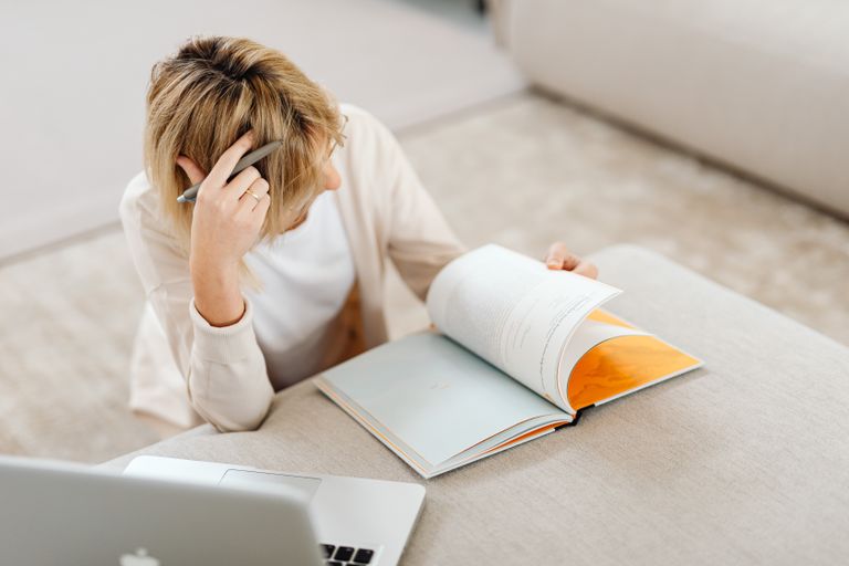 Blonde woman studying in living room with a book and laptop, creating a relaxed atmosphere.