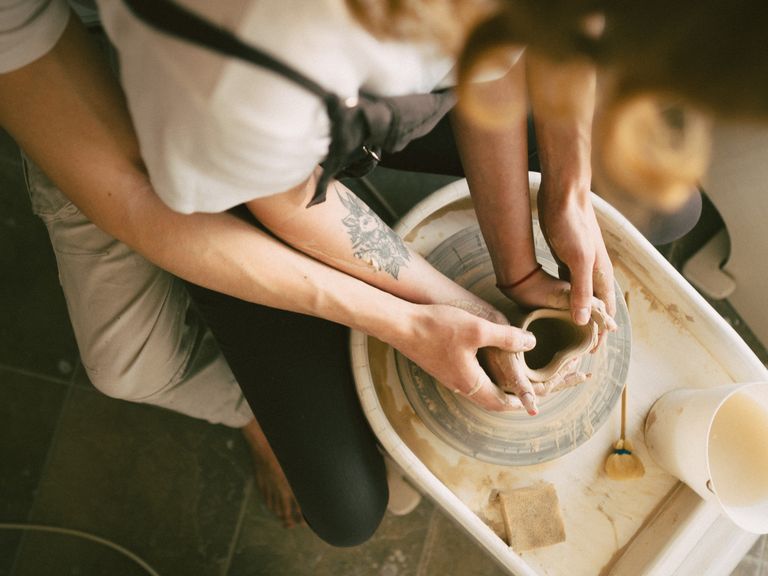 Close-up of two people shaping clay on a pottery wheel, creating art together.